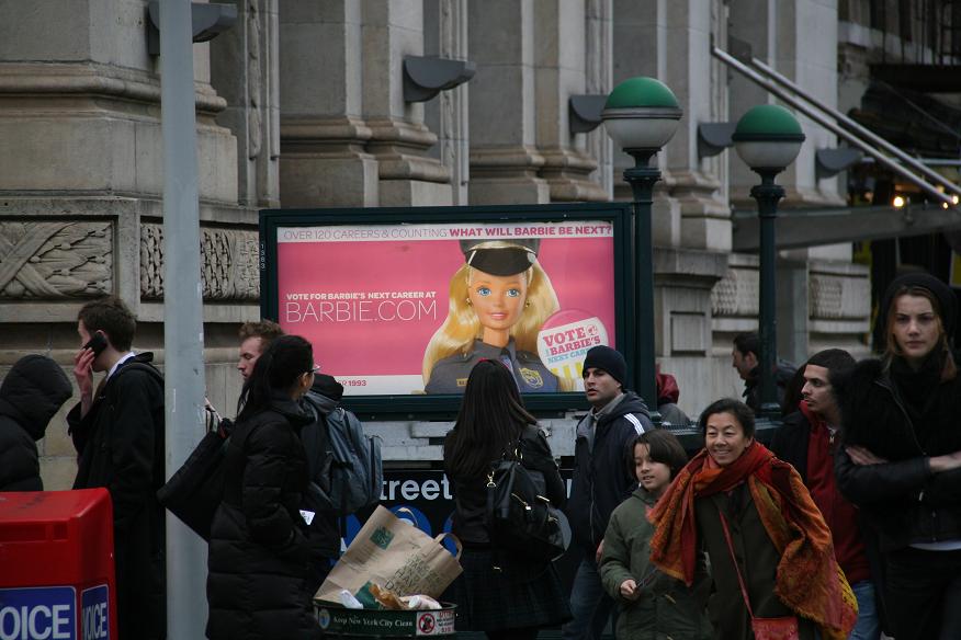 도시의 거리에서 유료 미디어 전문가가 제작한 바비 인형 광고를 지나가는 사람들.